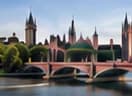 A stone road bridge over a river below a Gothic spired city landmark.