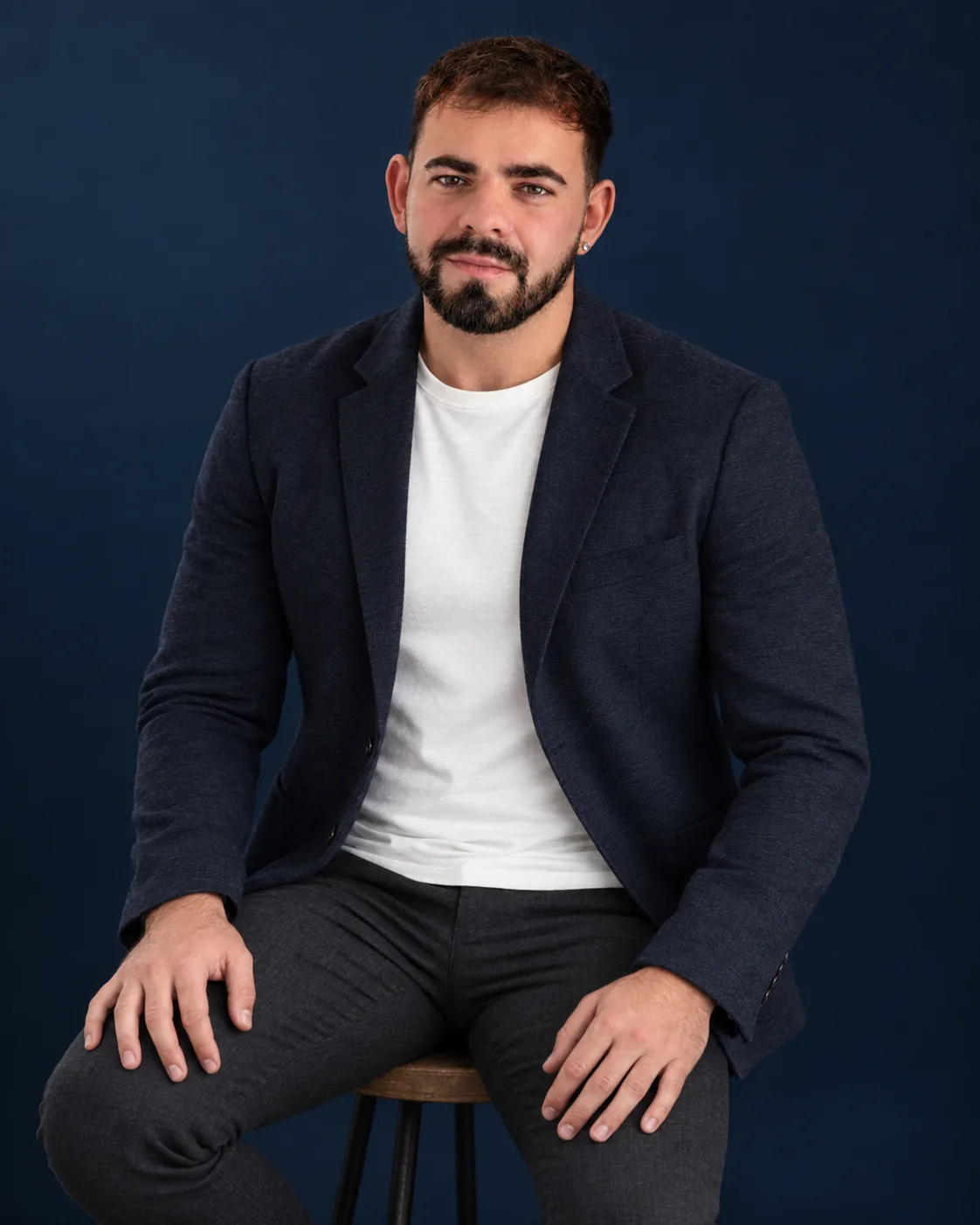 James Tandy seated in a navy jacket and white T-shirt against a deep navy background.